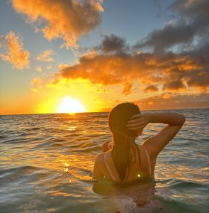 Woman in the ocean facing the sun rising.